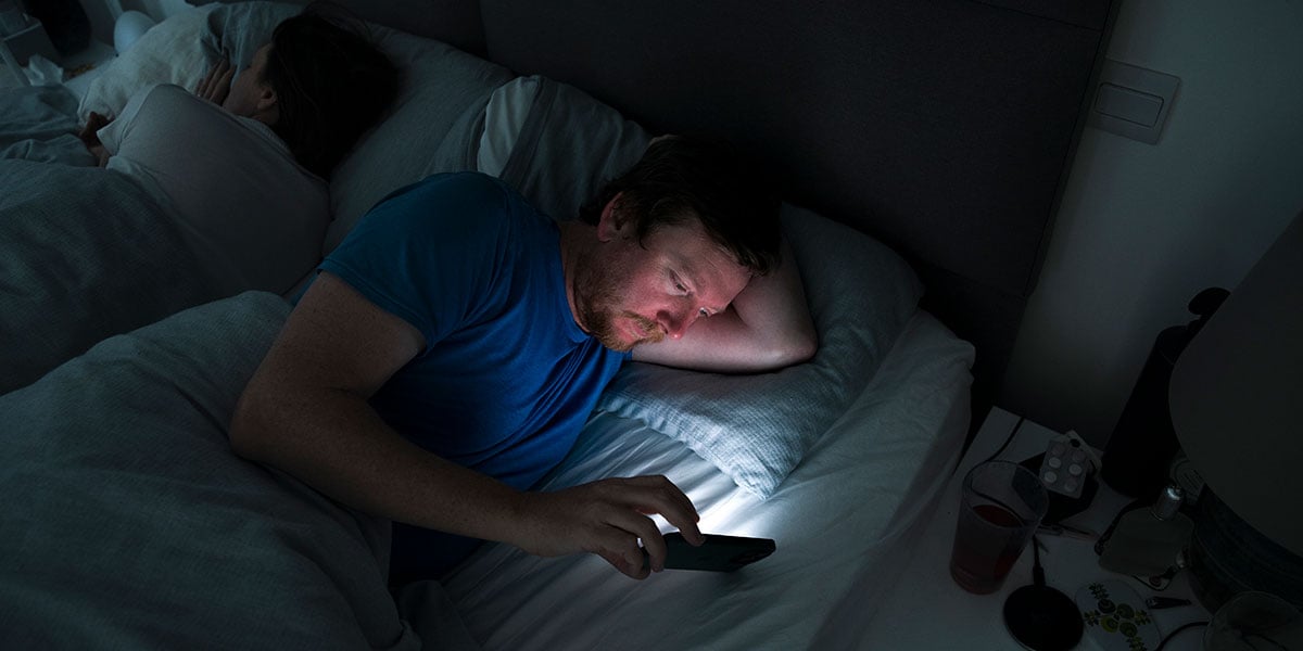 man on phone in bed insomnia