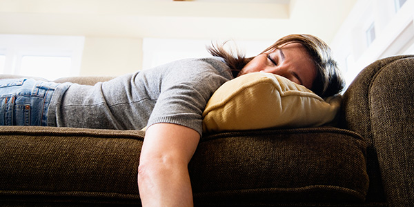 A middle-aged woman lies on a couch exhausted. Fatigue is caused by many things including poor sleep hygiene habits, lack of exercise and some conditions.