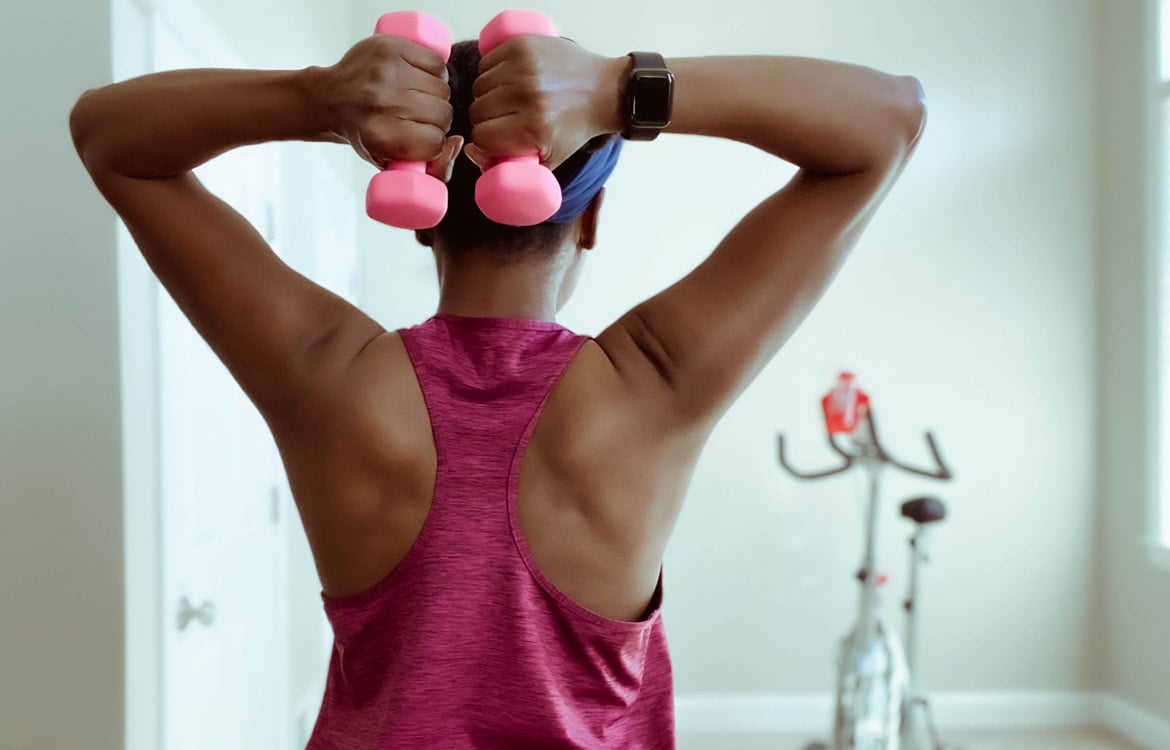 rear side view of woman lifting weights with both arms