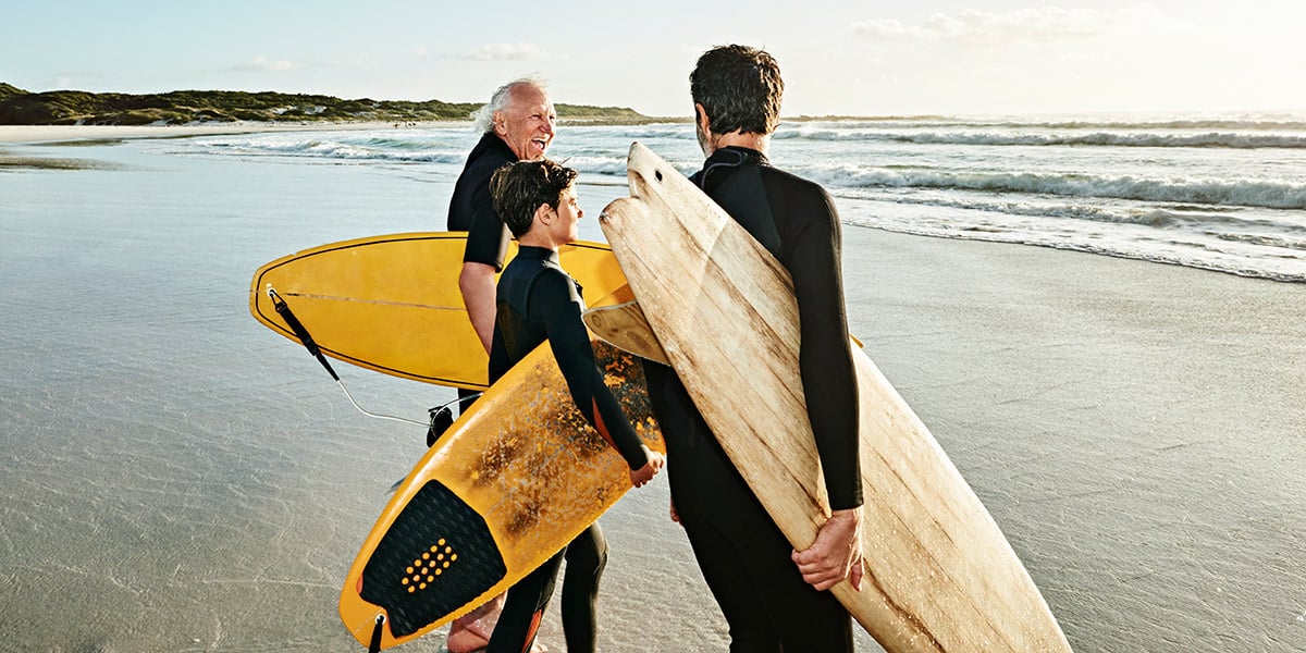 Two older men and a child holding surf boards