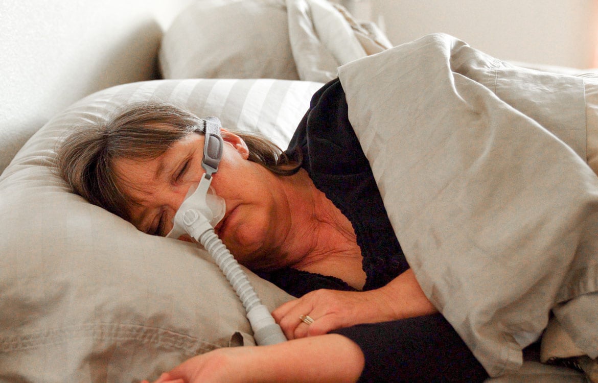 Older woman asleep in bed with a CPAP mask on