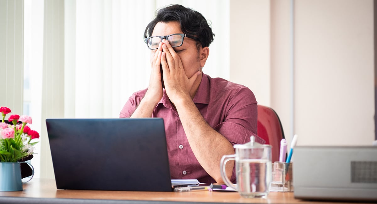 A man working at a computer is stressed and rubbing his eyes.