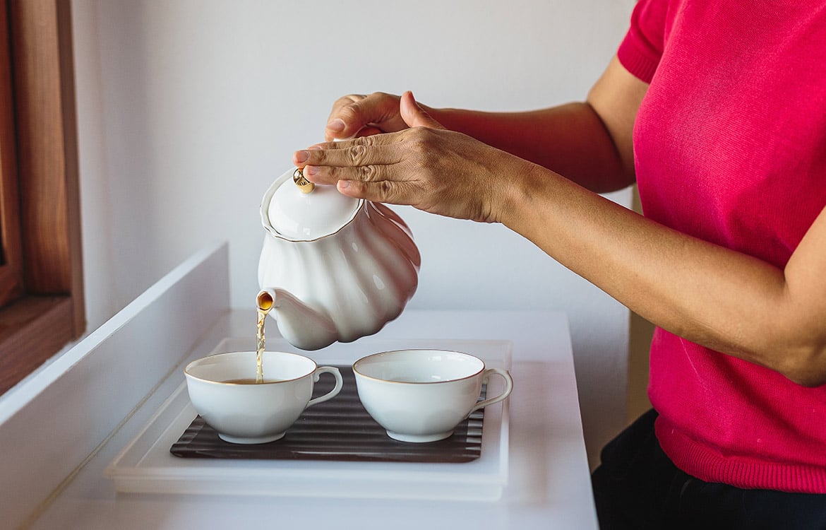 person pouring tea into teacup from tea kettle