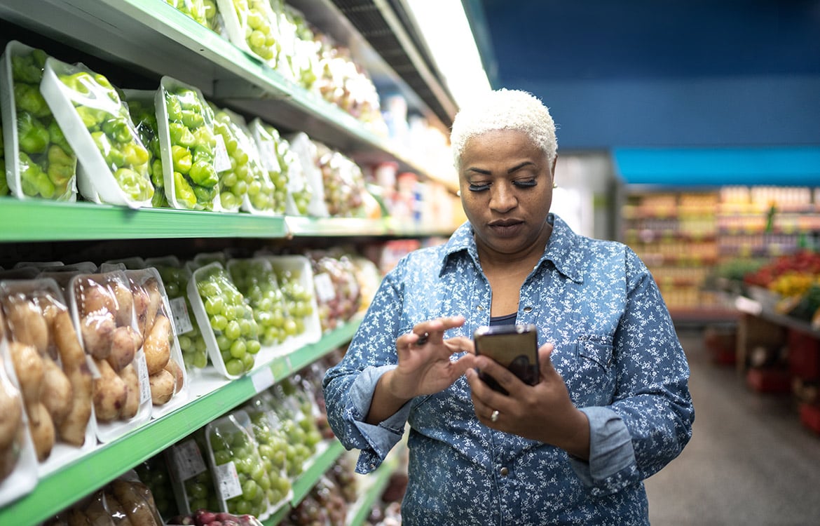 person using cellphone while standing next to produce section in grocery store