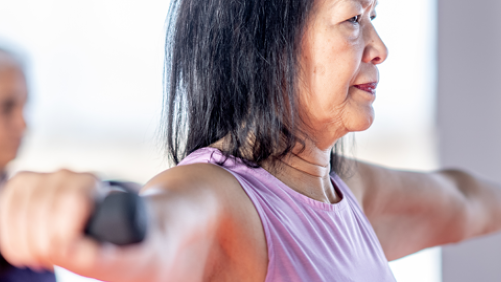 Older adults participate in a strength-training class, lifting dumbbells with arms extended during a group fitness session.