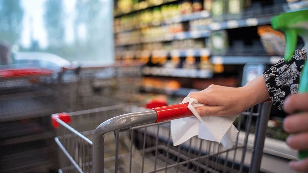 Woman wiping down grocery cart in supermarket