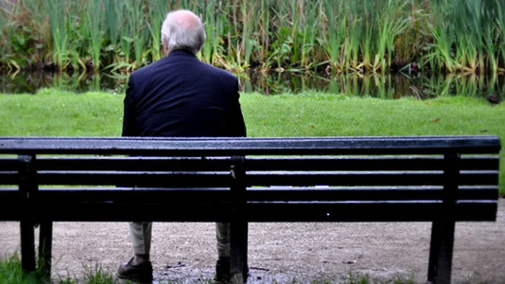 A man sits on a park bench by himself.