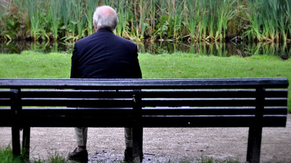 A man sits on a park bench by himself.