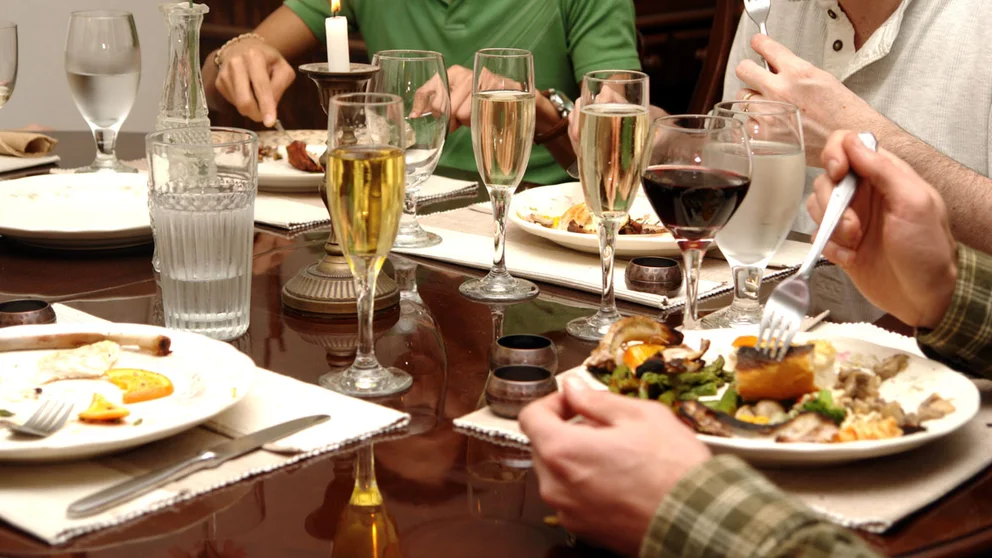 Family eating at dining table with full plate, champagne, and wine