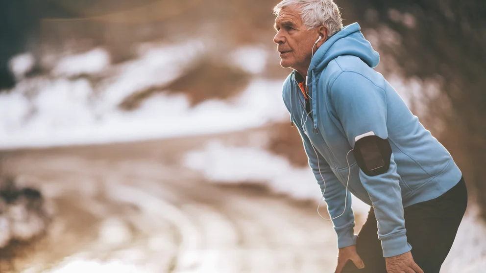 older man listening to music taking a break from running during the winter