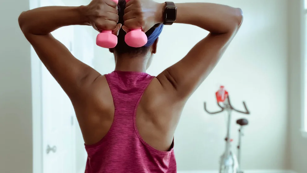 rear side view of woman lifting weights with both arms