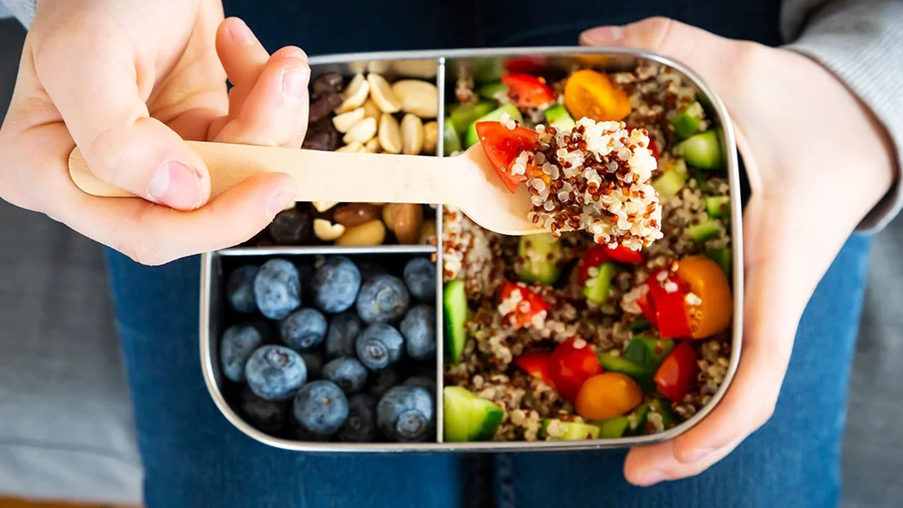 Person using spoon to lift fruit, nuts, vegetables and grains from a food tray