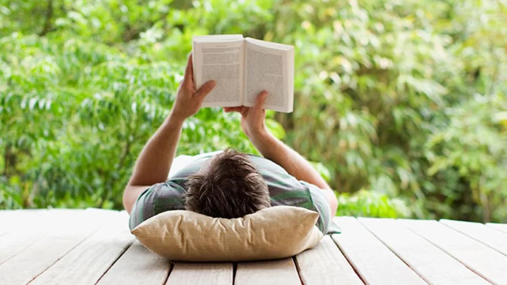 Man on a porch, laying on his back reading a book