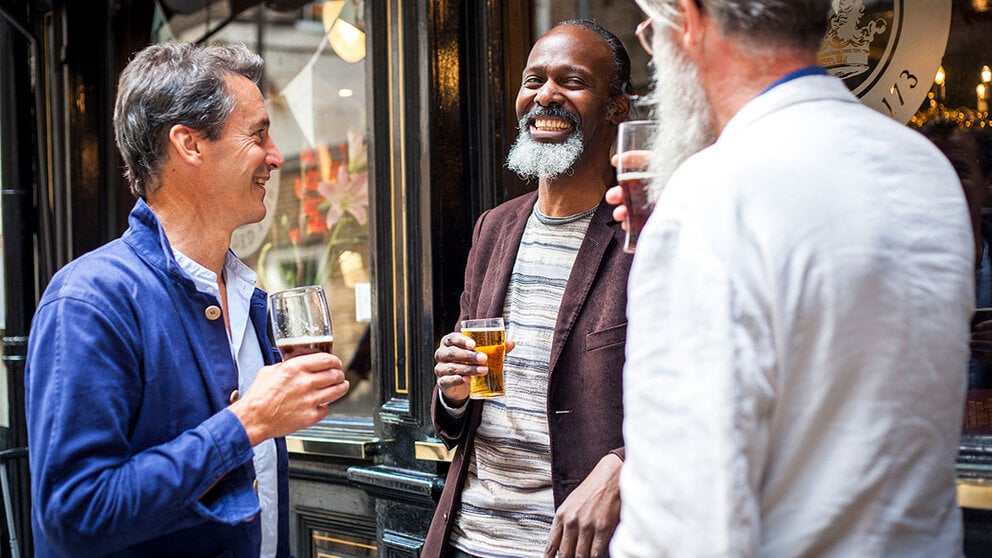 Three men drinking beer in front of a pub.