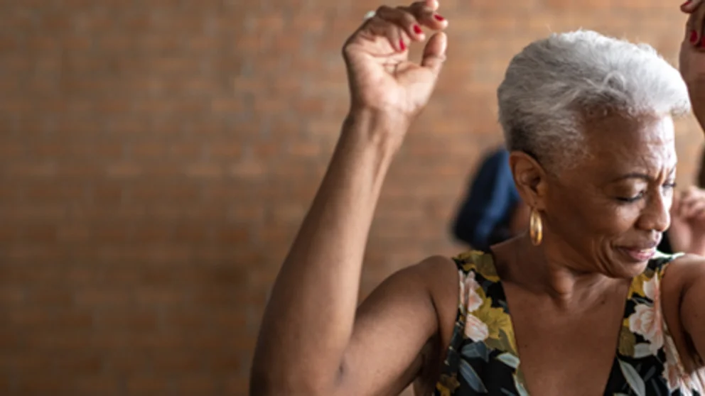 Woman dancing with her arms and hands in the air with a brick wall in the background
