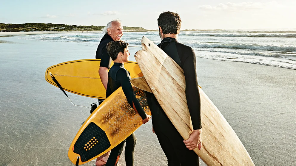 Two older men and a child holding surf boards