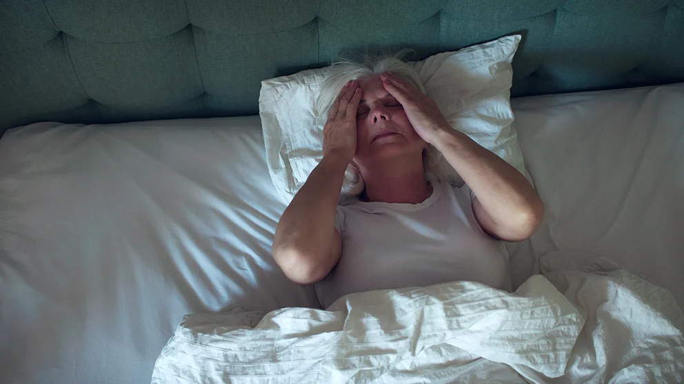 older woman laying in bed gripping sides of head