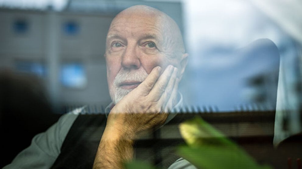 An older man stares out a window alone.