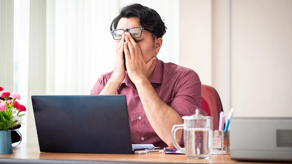 A man working at a computer is stressed and rubbing his eyes.