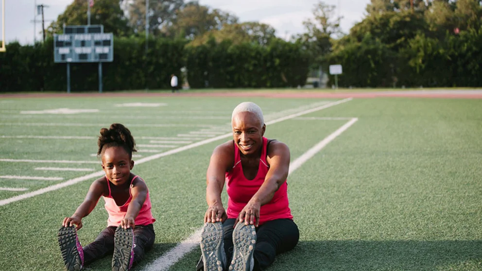 Grandmother and granddaughter stretching on football field