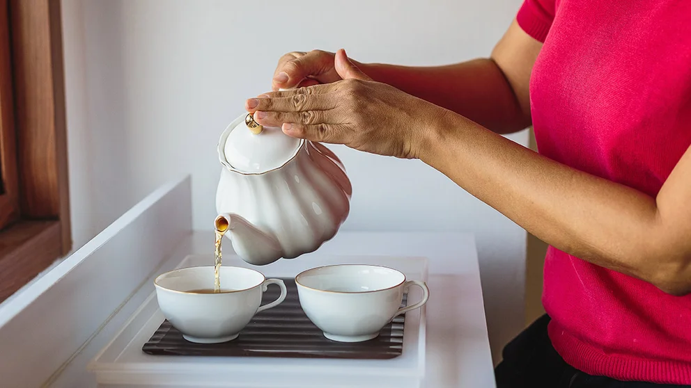 person pouring tea into teacup from tea kettle