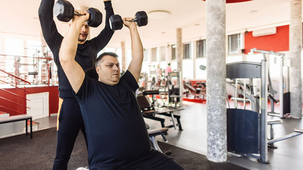 Trainer spotting man during overhead press with dumbbells