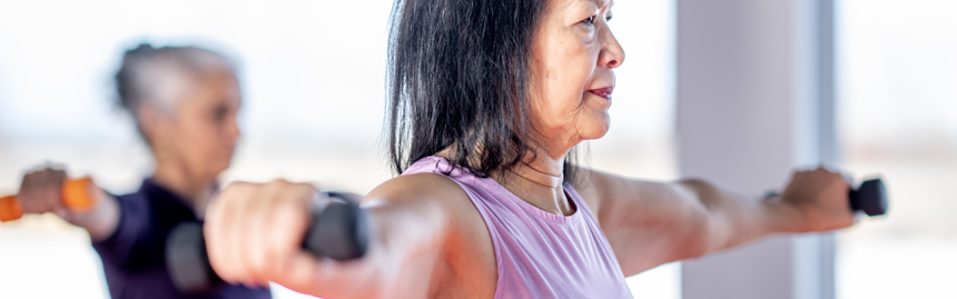 Older adults participate in a strength-training class, lifting dumbbells with arms extended during a group fitness session.