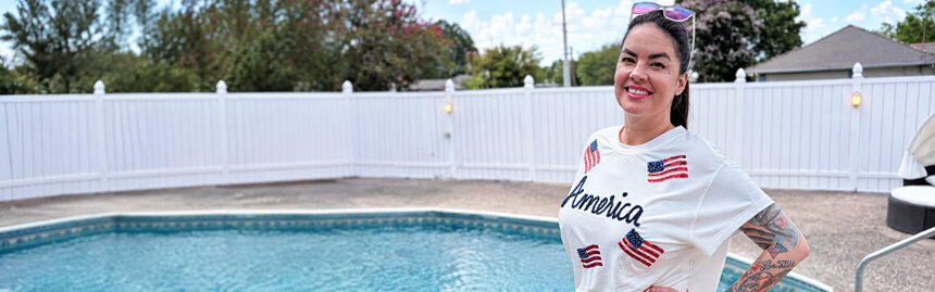 Smiling woman with colorful tattoos standing beside a backyard swimming pool.