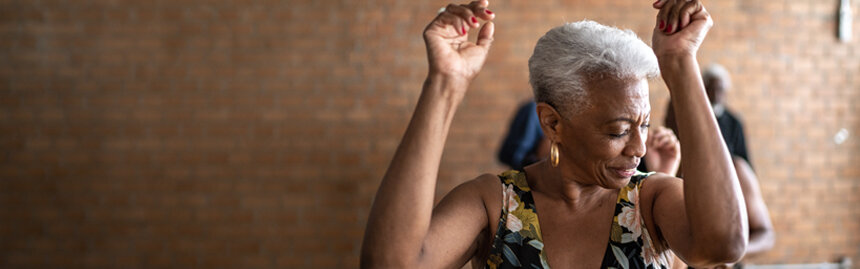 Woman dancing with her arms and hands in the air with a brick wall in the background