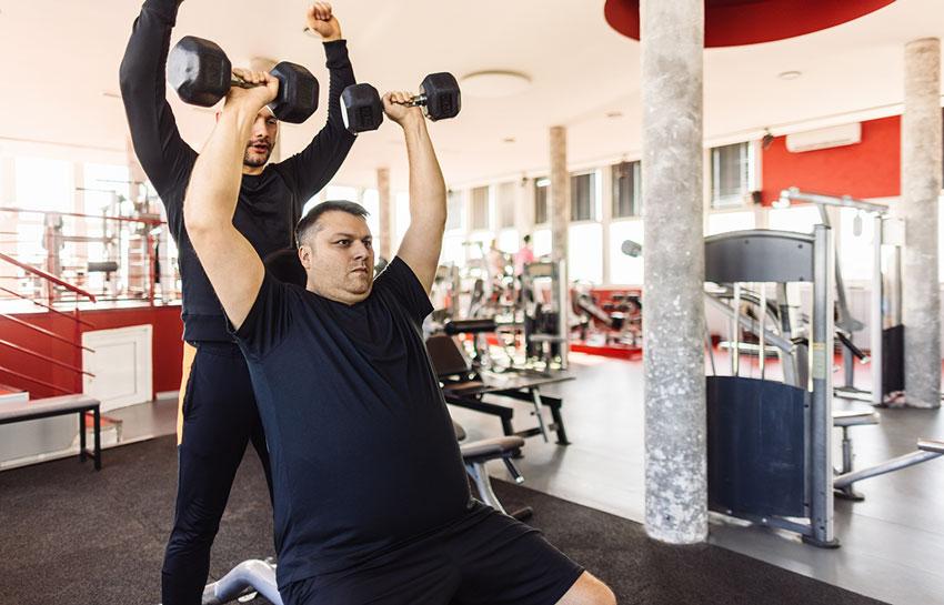 Trainer spotting man during overhead press with dumbbells