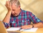 older man sitting at desk in pain with his hand on forehead