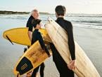 Two older men and a child holding surf boards