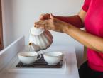 person pouring tea into teacup from tea kettle