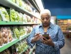 person using cellphone while standing next to produce section in grocery store