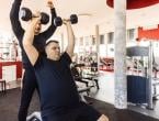 Trainer spotting man during overhead press with dumbbells