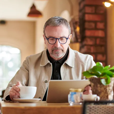 mature-man-looking-at-tablet-while-holding-cup-of-coffee
